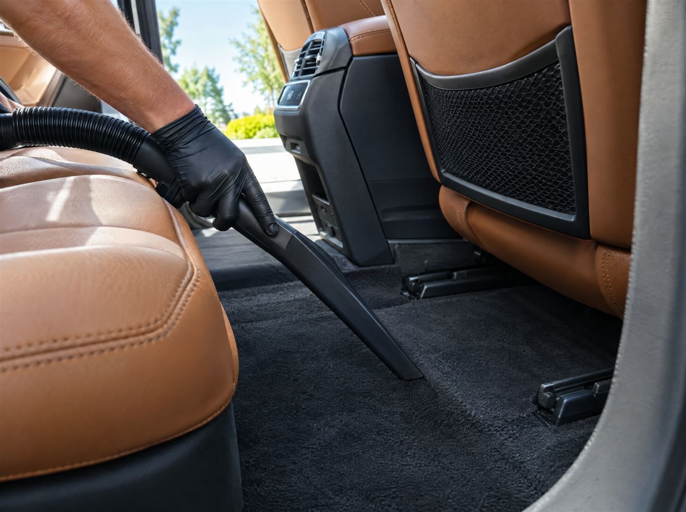 Detailer vacuuming the carpet of a car interior with tan leather seats